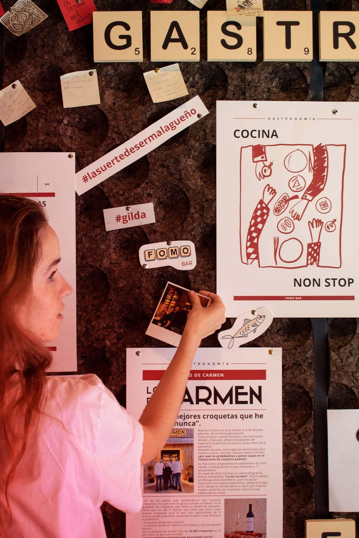 A customer pins a note on FOMO Bar’s cork board, next to the «COCINA NON STOP» menu poster.