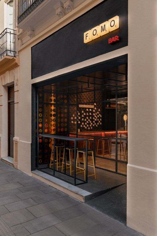 Fachada de FOMO Bar en la calle Carretería: banda negra con el rótulo de fichas y la cristalera abierta a la sala.