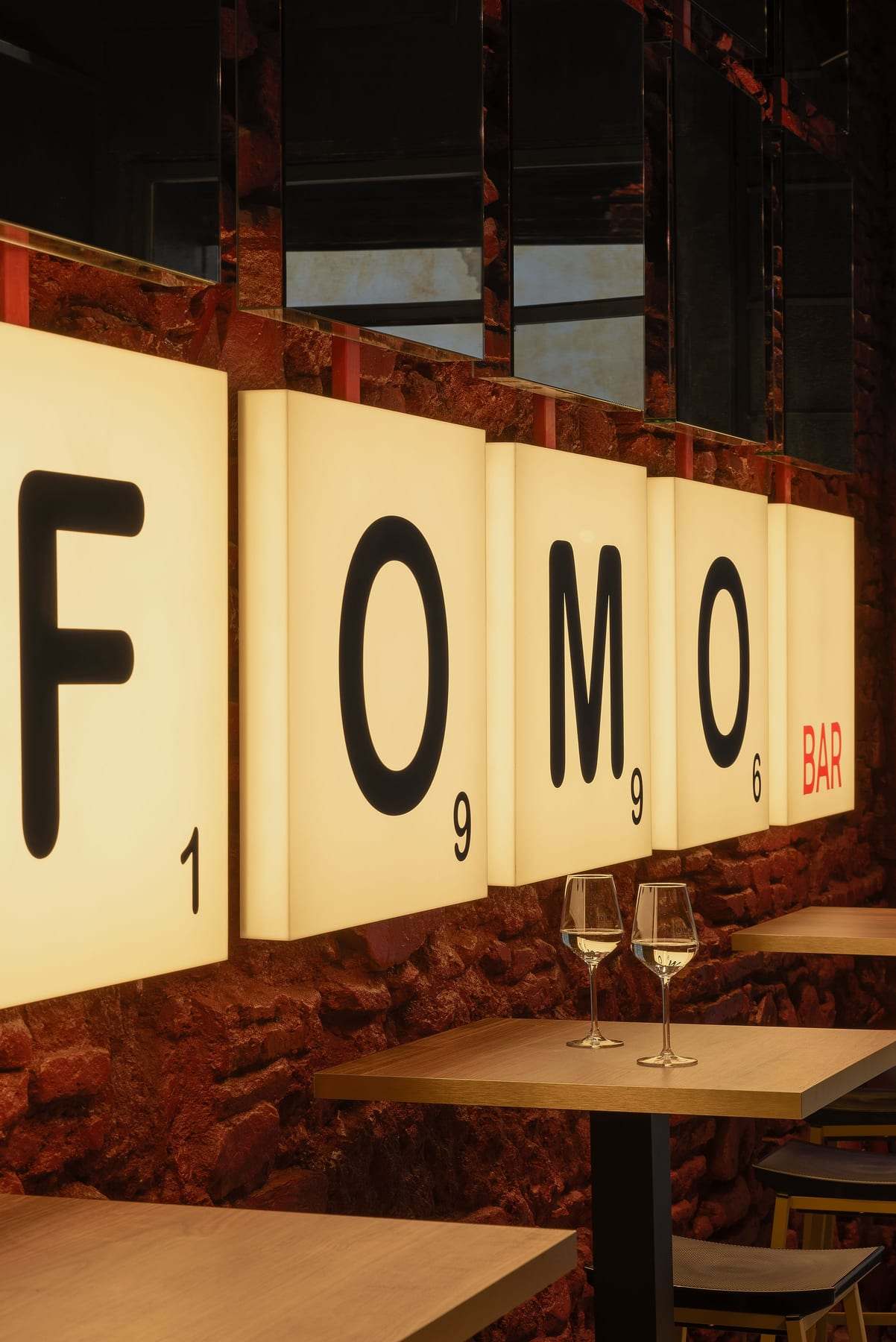 FOMO light boxes on the red stone wall, with high wooden tables and wine glasses.