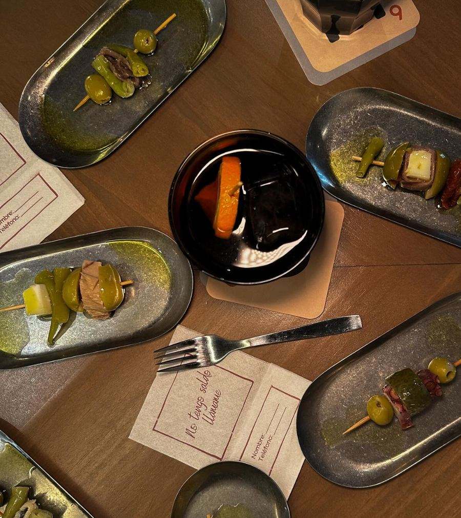 Overhead view of a FOMO Bar table with several gildas on small metal trays, a vermouth with orange and “No tengo saldo. Llámame” napkins.