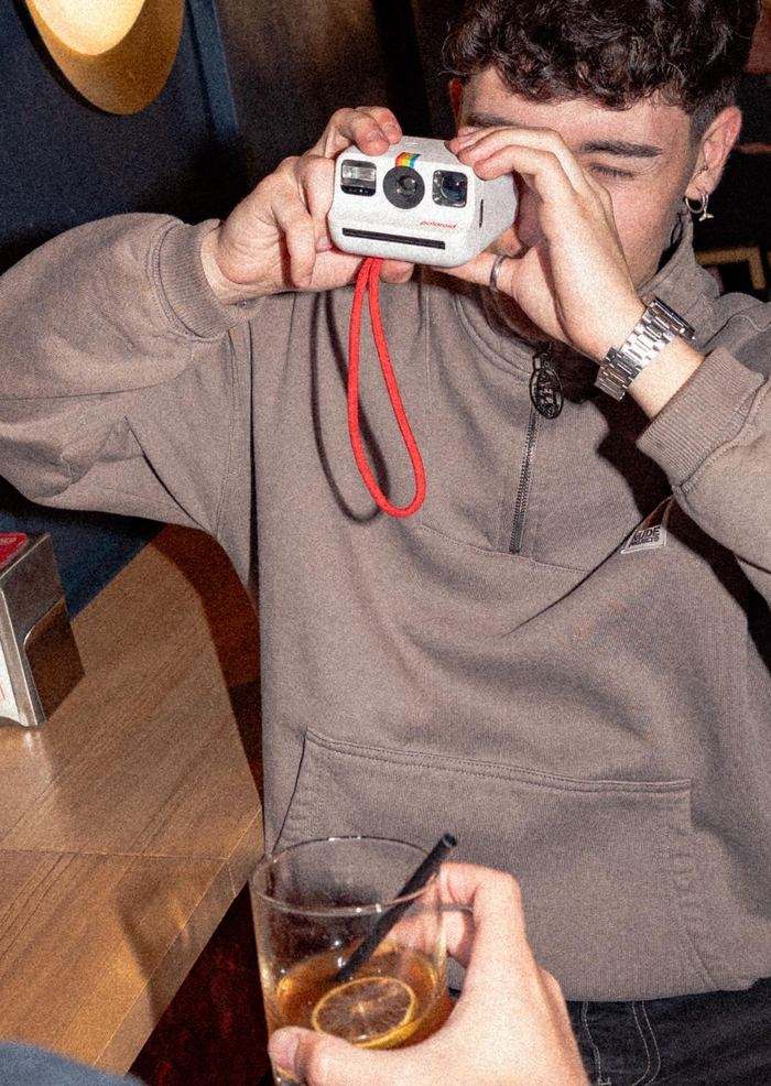 A customer takes a photo with a Polaroid camera at the bar, with direct flash and a vermouth in the foreground.