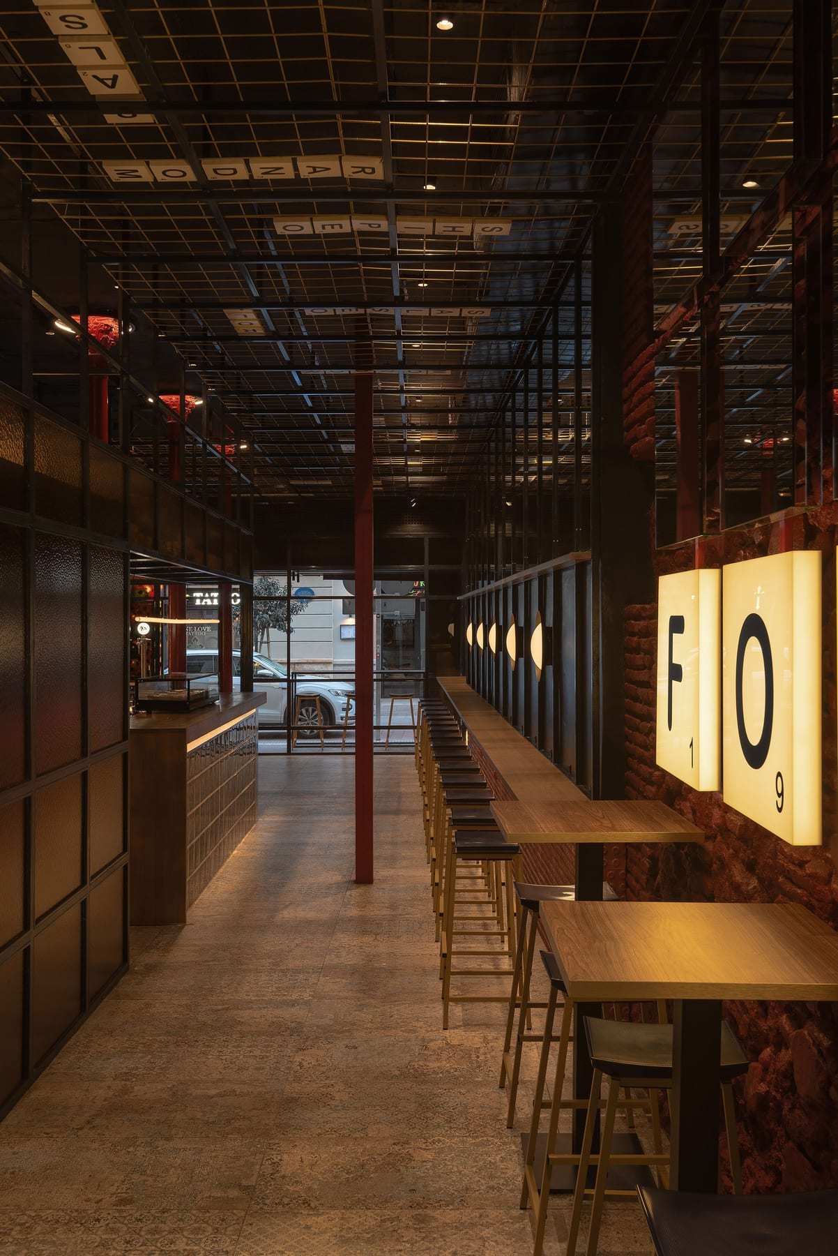 FOMO Bar’s long room with high tables and stools, the F and O light boxes on the wall and the black grid ceiling.