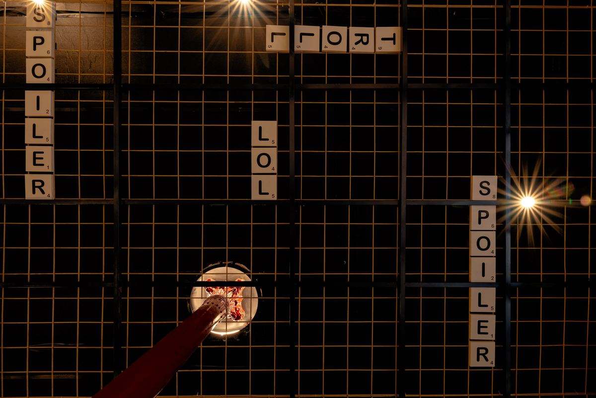 Black grid ceiling with the words SPOILER, LOL and TROLL spelled in hanging letter tiles and lit spotlights.